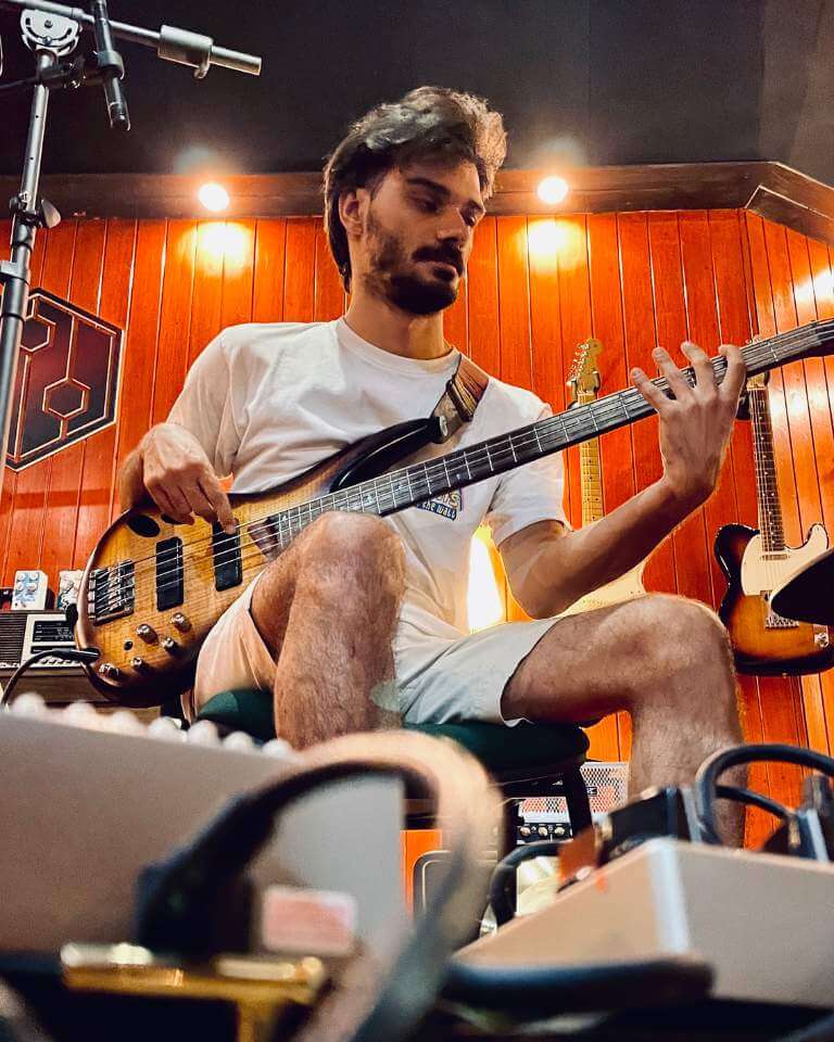 A bass player focused during a recording session in a professional studio, with warm wooden walls and guitars in the background.