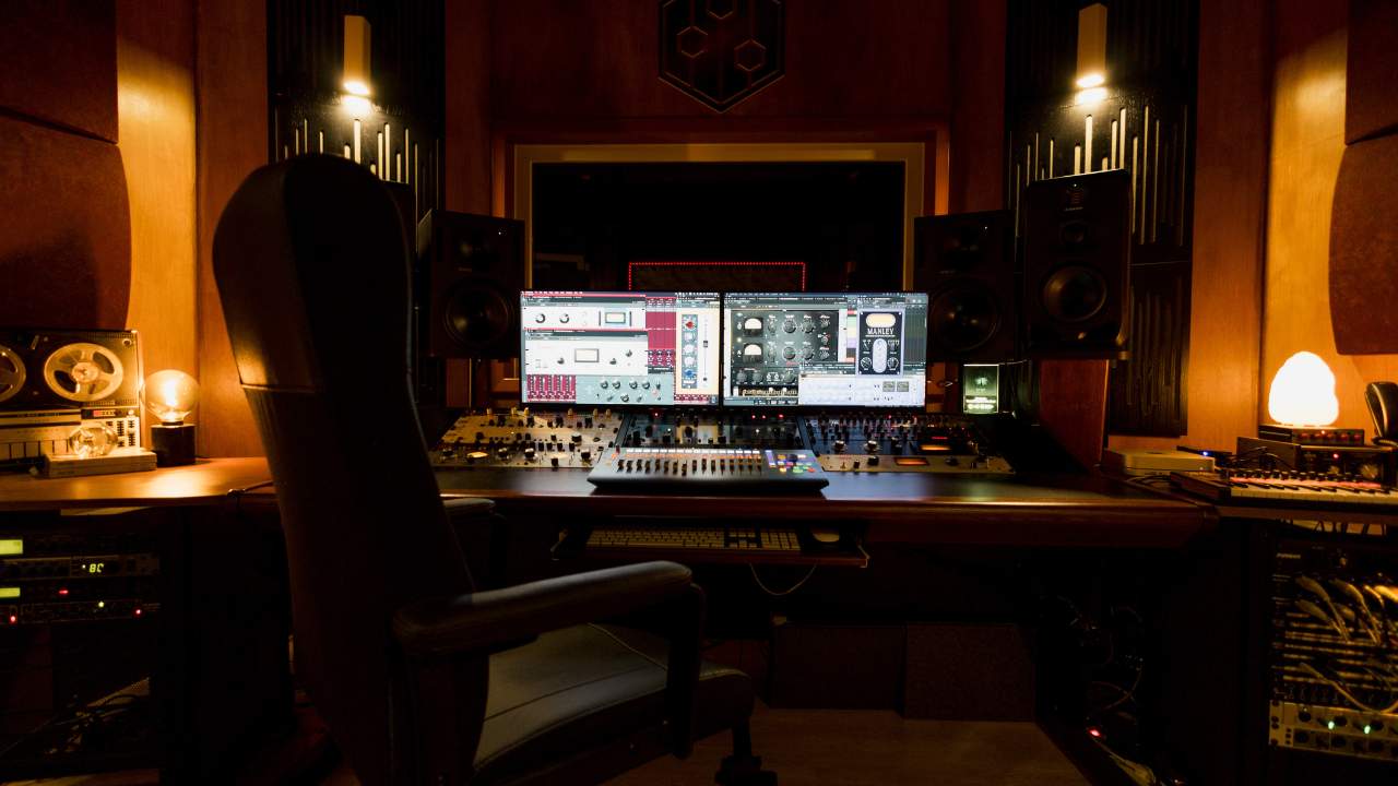 Sound Pressure Studios control room featuring a professional audio setup with dual monitors, mixing console, speakers, and warm ambient lighting.
