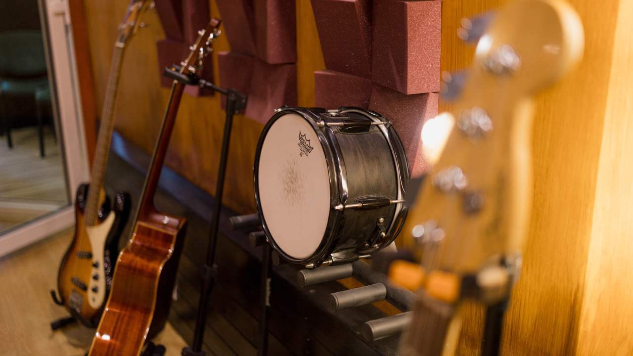 A collection of studio instruments, including a bass guitar, acoustic guitar, and snare drum, against a backdrop of acoustic foam panels.